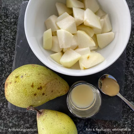 ganze Birnen, Birnenstücke, Zitronensaft im Glas, Honig auf dem Löffel auf einer Schiefertafel angerichtet