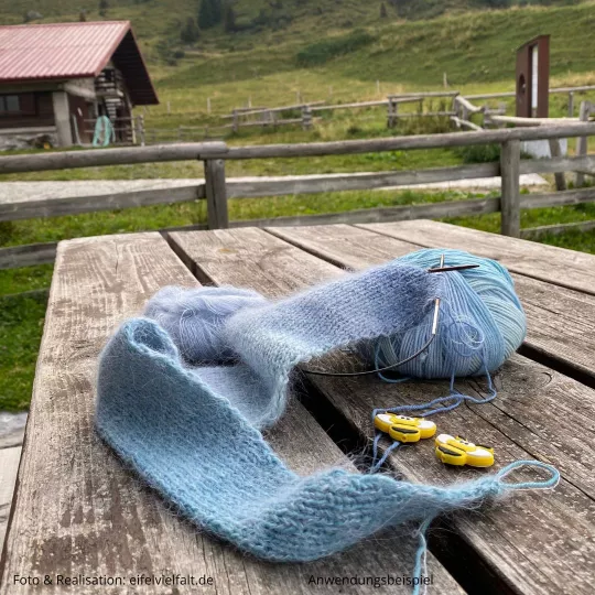 Dreiecksschal in Strickarbeit liegend auf einem Holztisch auf einer Alm mit Blick auf die Berge