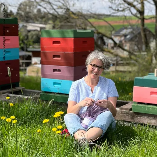 Strickende Frau sitzt vor Bienenstöcken auf der Wiese