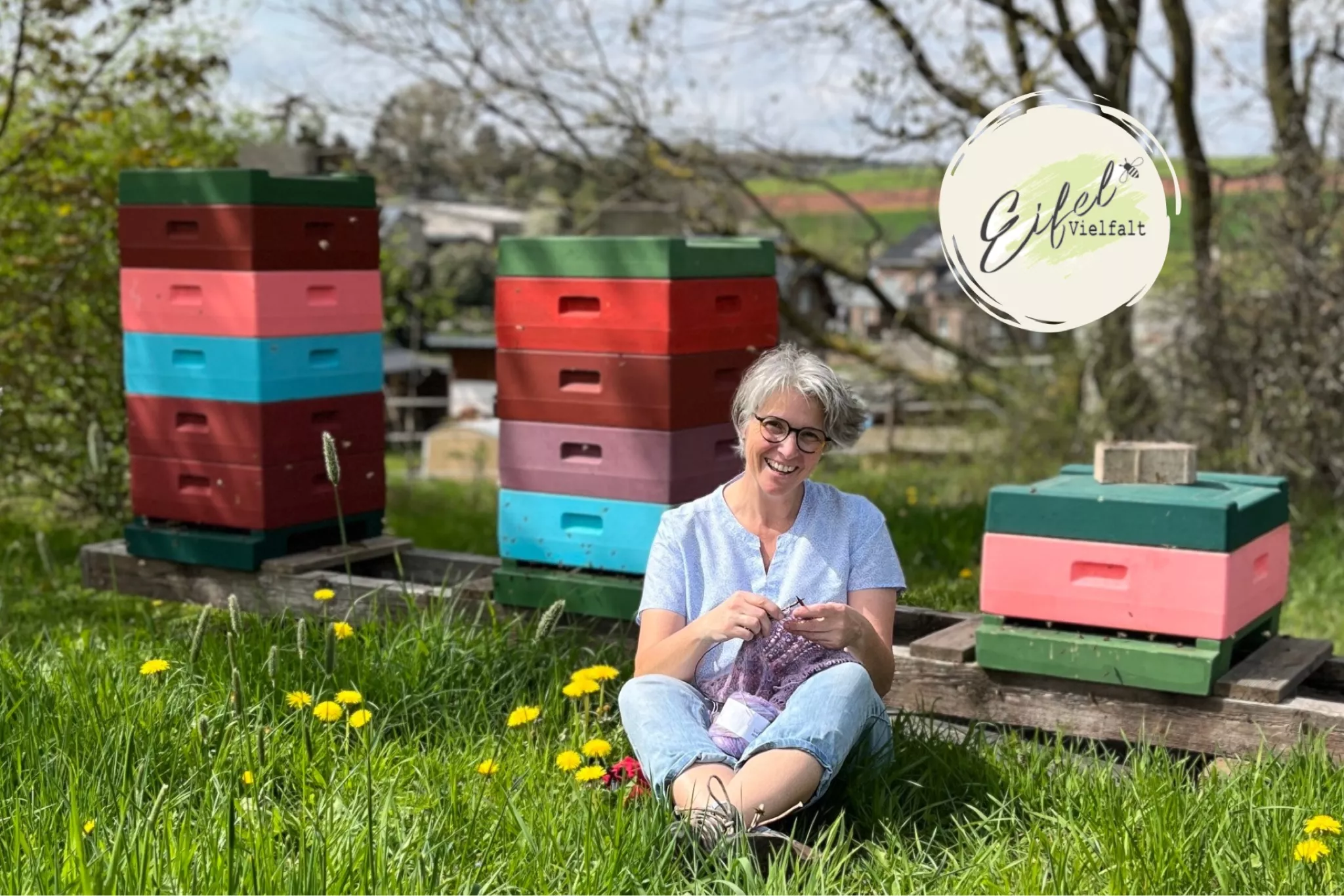 Susanne Blens  strickend vor Bienenkästen im Gras sitzend