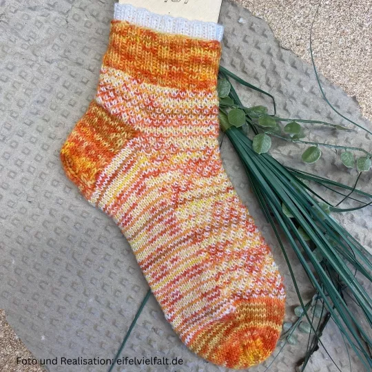 Sneakersocke in orange-gelb-weiß-Tönen auf Sockenlineal aufgezogen