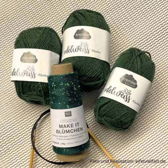 3 Knäuel Kremke Alpaka Edelweiß in tannengrün und 1 Kone Make-it-Blümchen in Efeu und eine passende Stricknadel liegen auf einem weißen Hintergrund