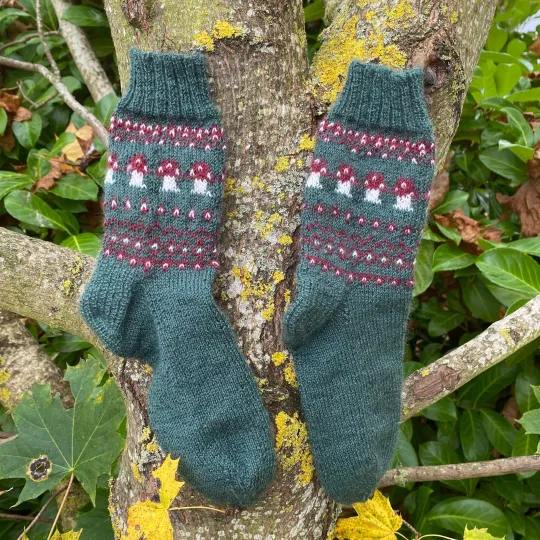 Stricksocken in tannengrün mit Pilzmuster hängen am Baum